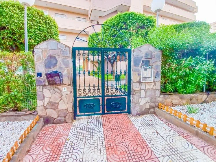 Una puerta metálica ornamentada entre pilares de piedra da a un patio ajardinado.