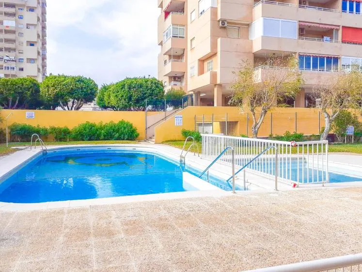 Una piscina al aire libre está junto a edificios de apartamentos y vegetación ajardinada.