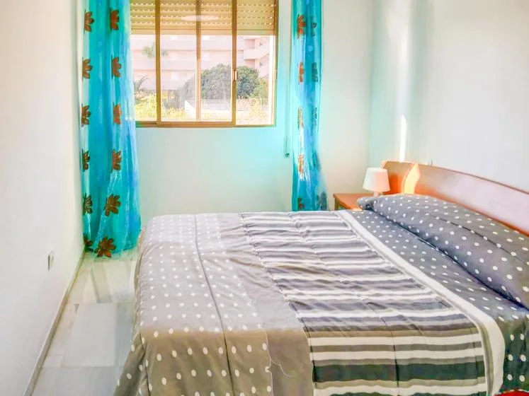 Un dormitorio con una cama, ropa de cama estampada y una ventana con cortinas azules.