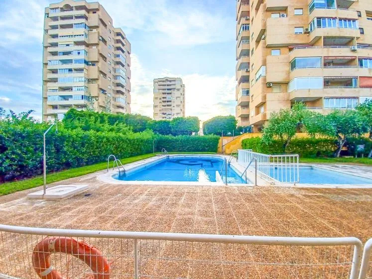 Una piscina al aire libre está rodeada de setos y edificios de apartamentos.