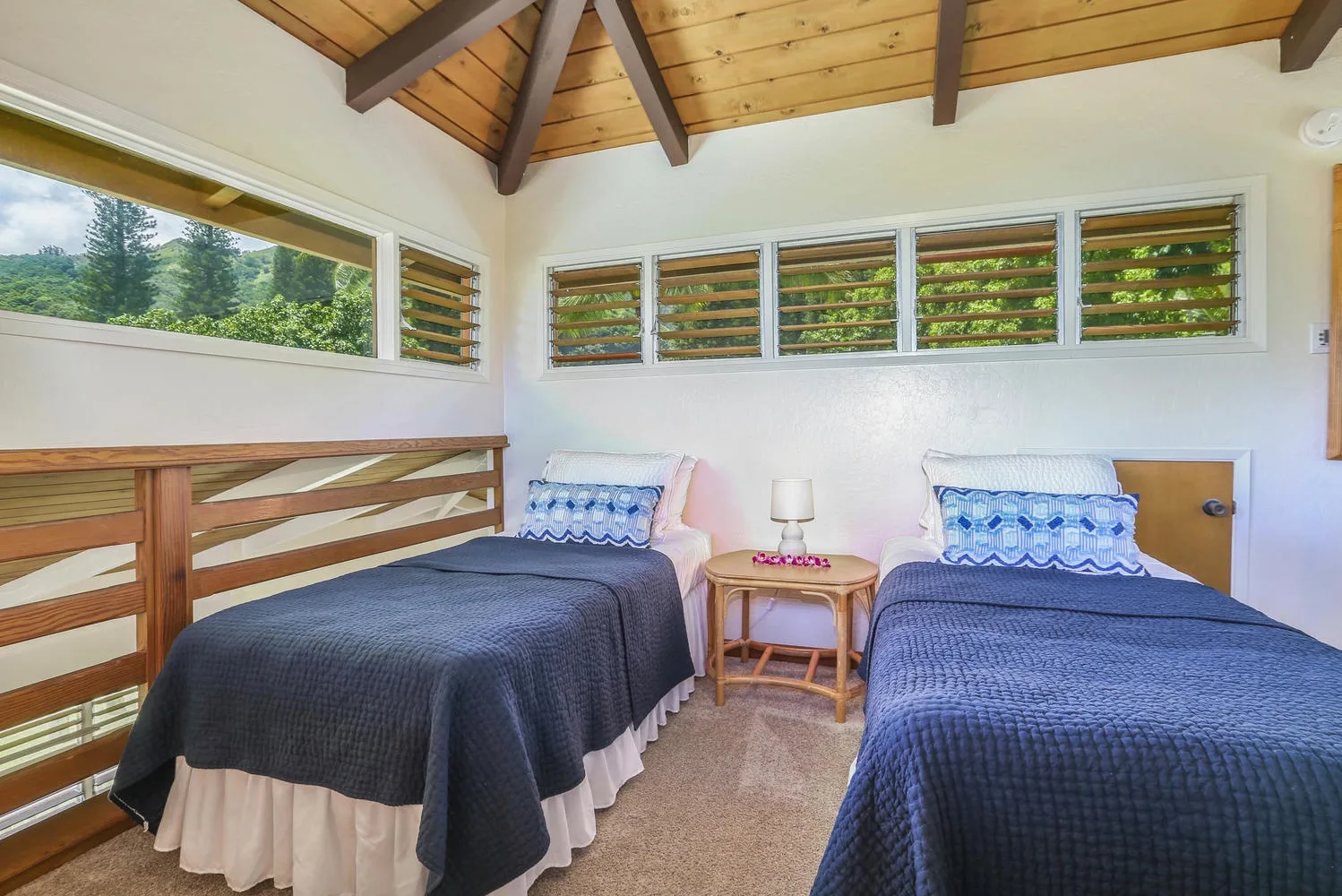 A bedroom with two beds beneath a wood-paneled ceiling and high windows.