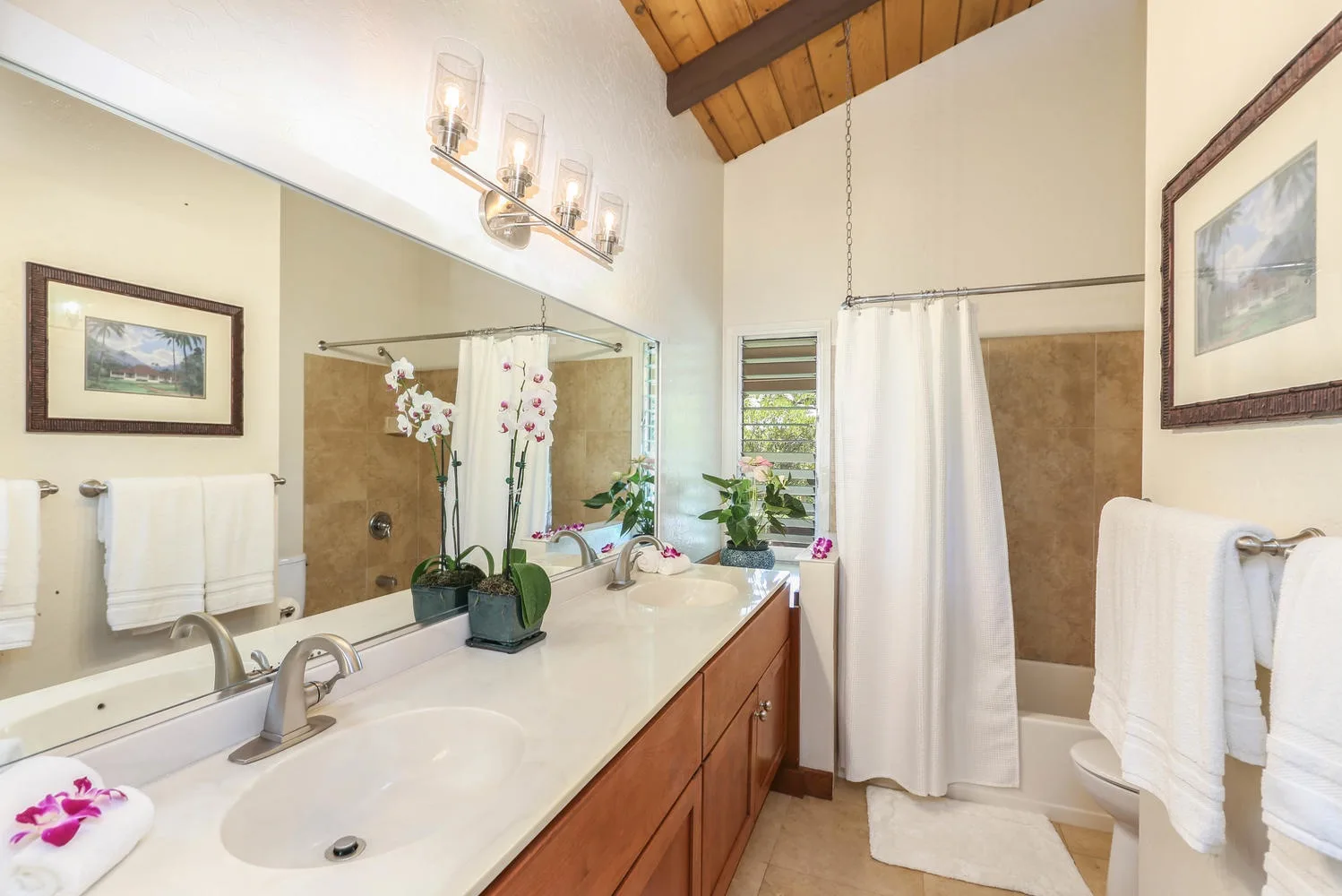 A bright bathroom with a long vanity, large mirror, and curtained bathtub.