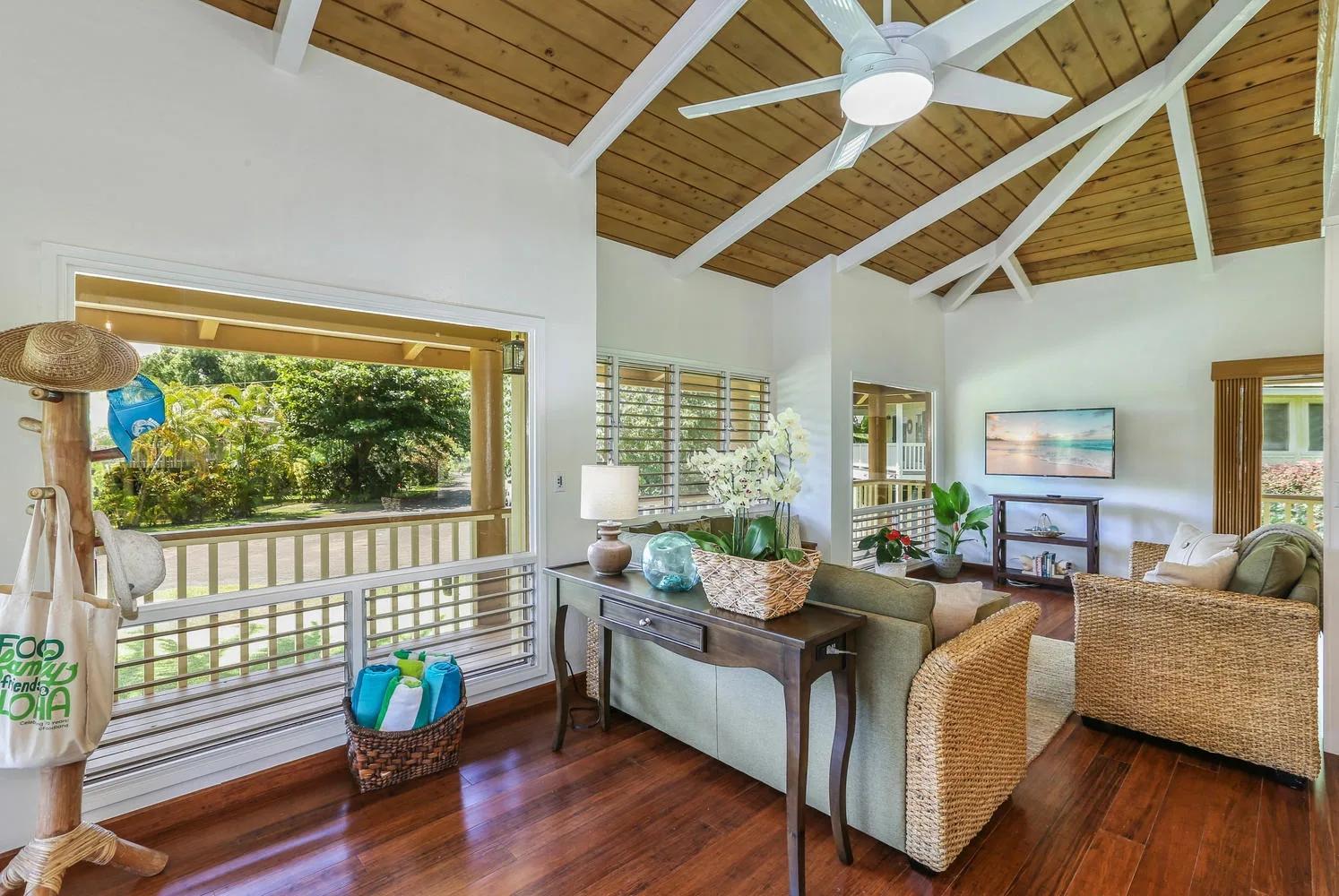 A bright living room with a high wood-paneled ceiling and wicker seating.