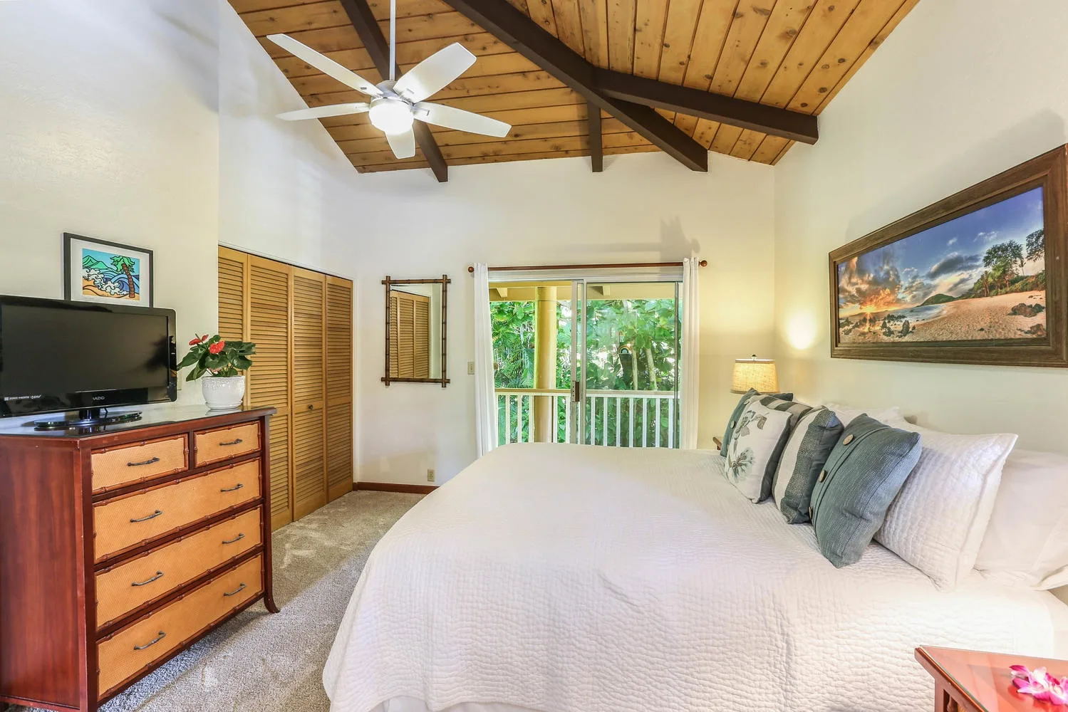 A bedroom with a large bed beneath a vaulted wood ceiling and a ceiling fan.