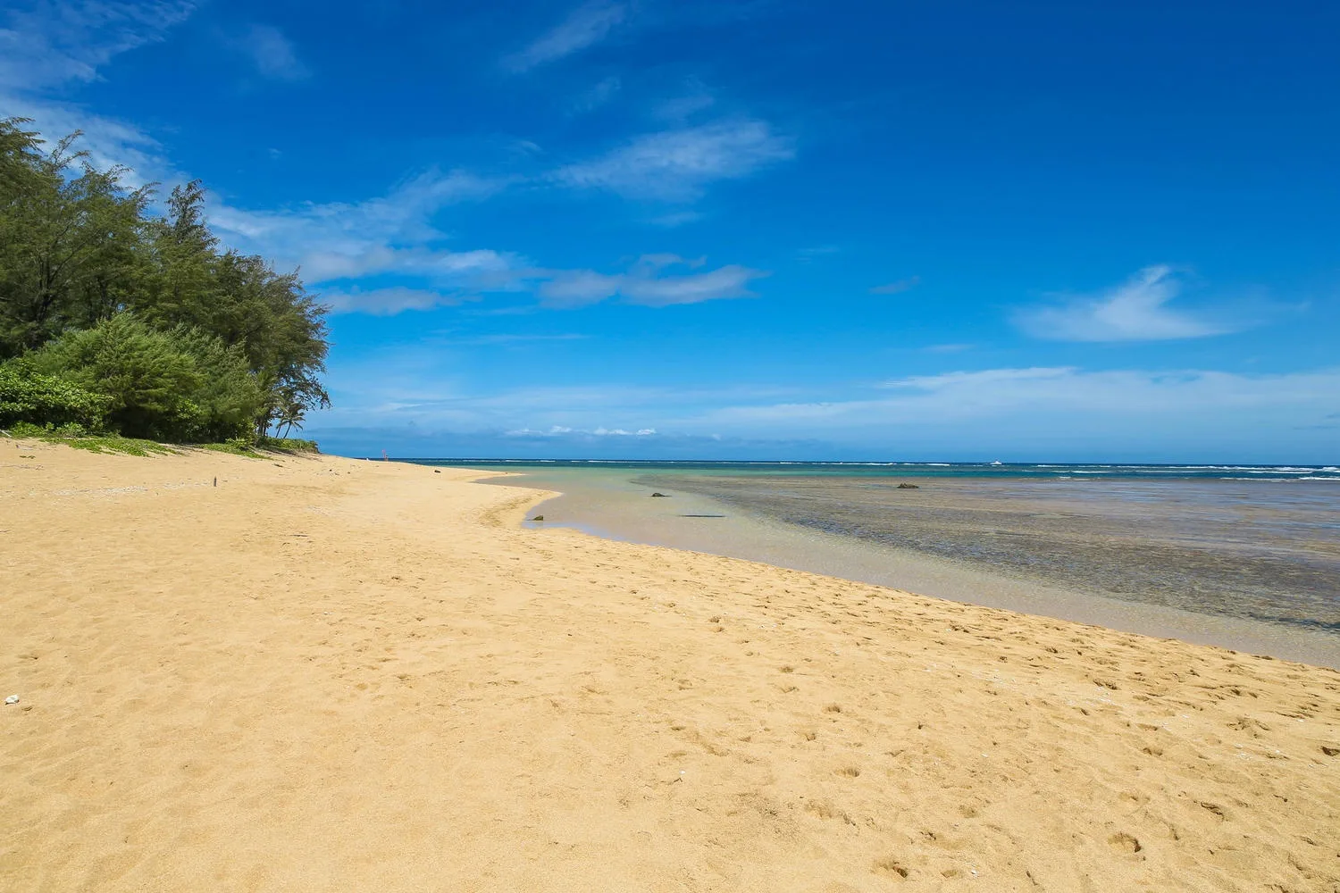 A sandy beach curves beside shallow water under a blue sky.