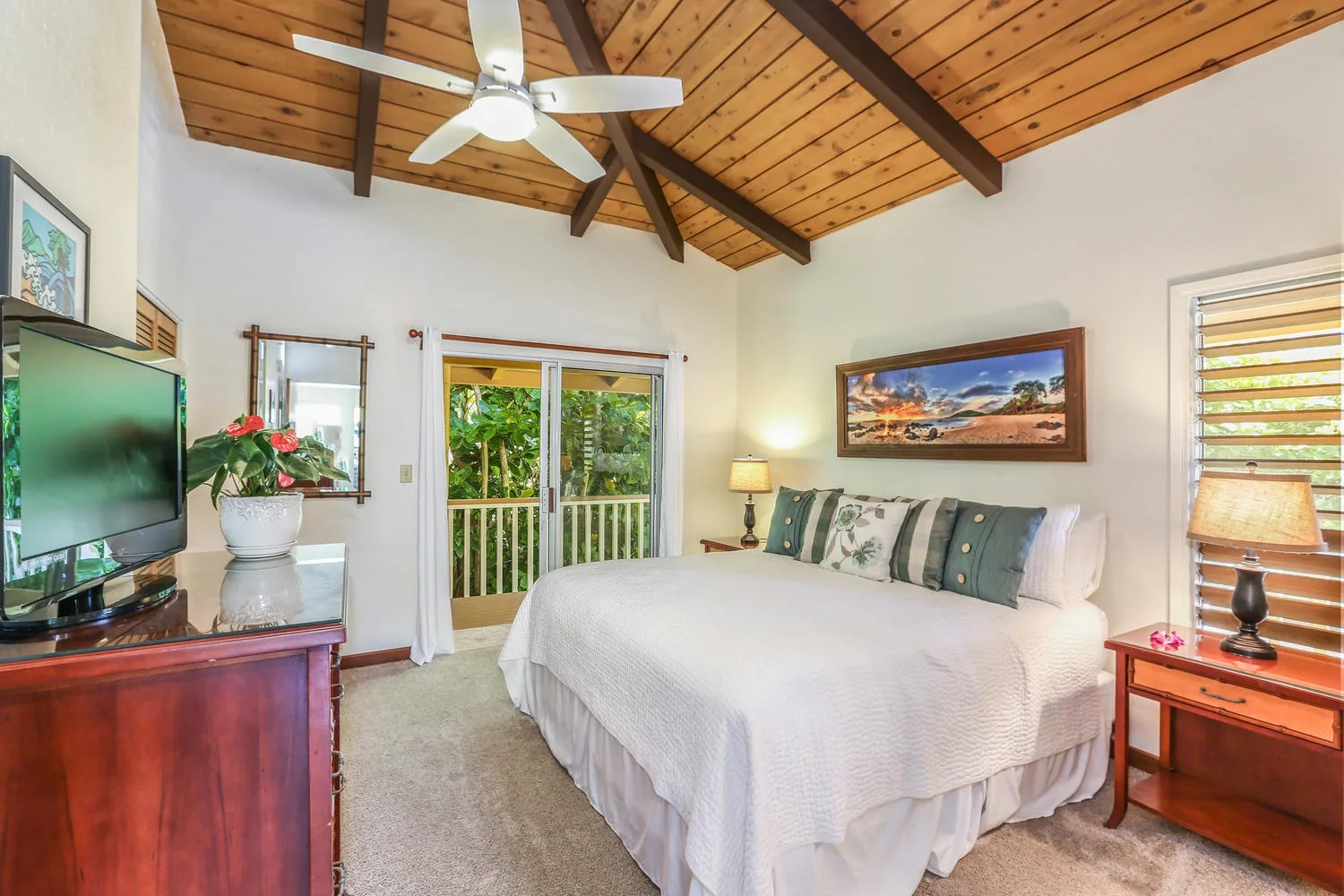 A bedroom with a large bed beneath a sloped wooden ceiling and ceiling fan.