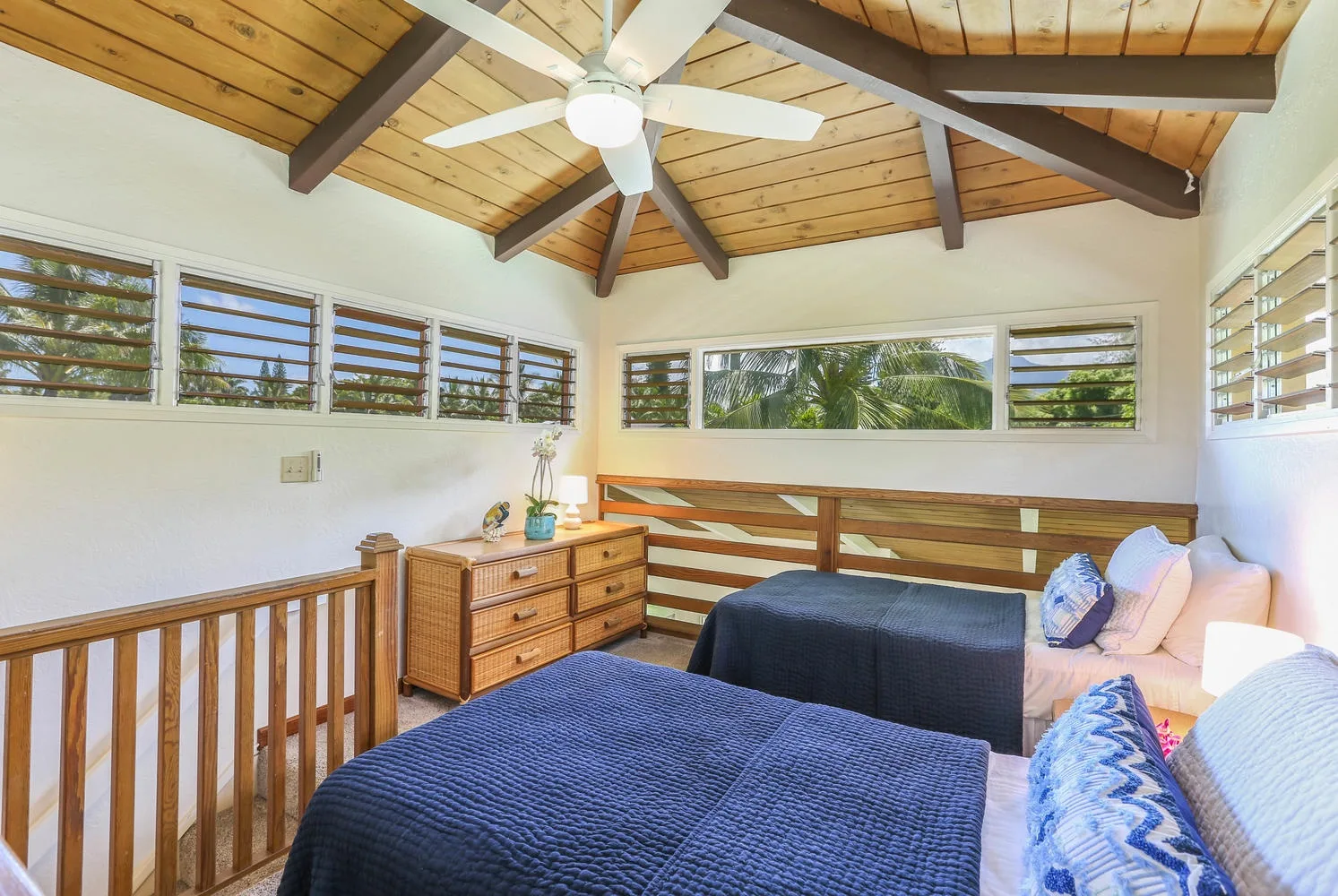 A bedroom with beds and a wooden railing beneath a beamed ceiling.