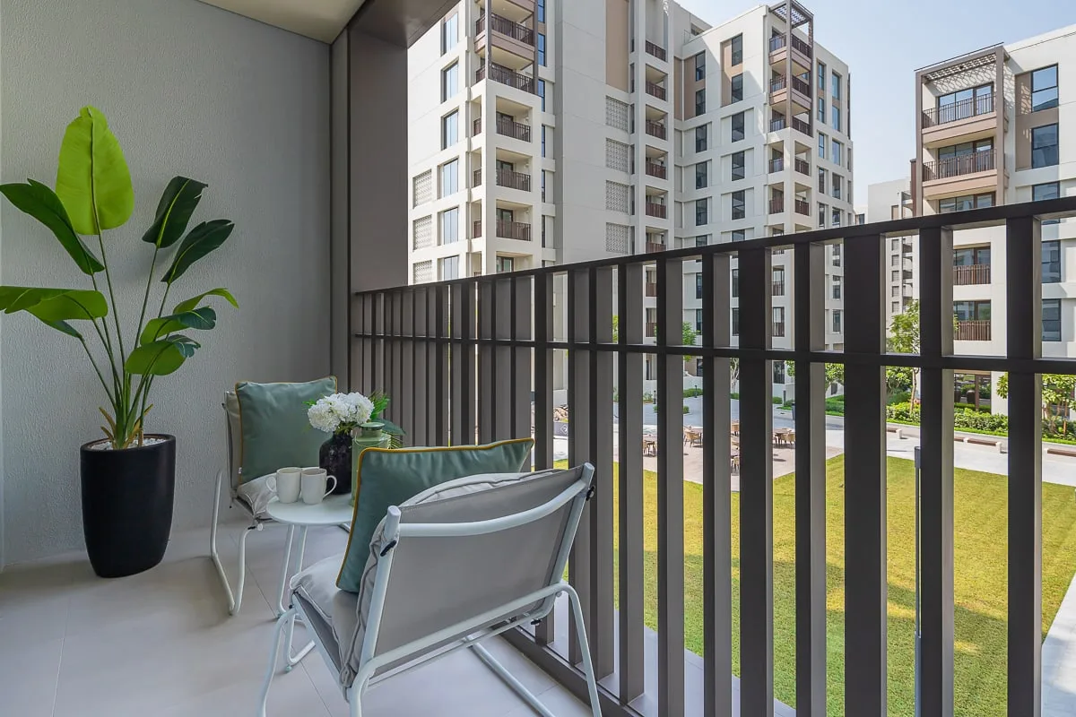 A balcony seating area overlooks landscaped grounds and nearby apartment buildings.