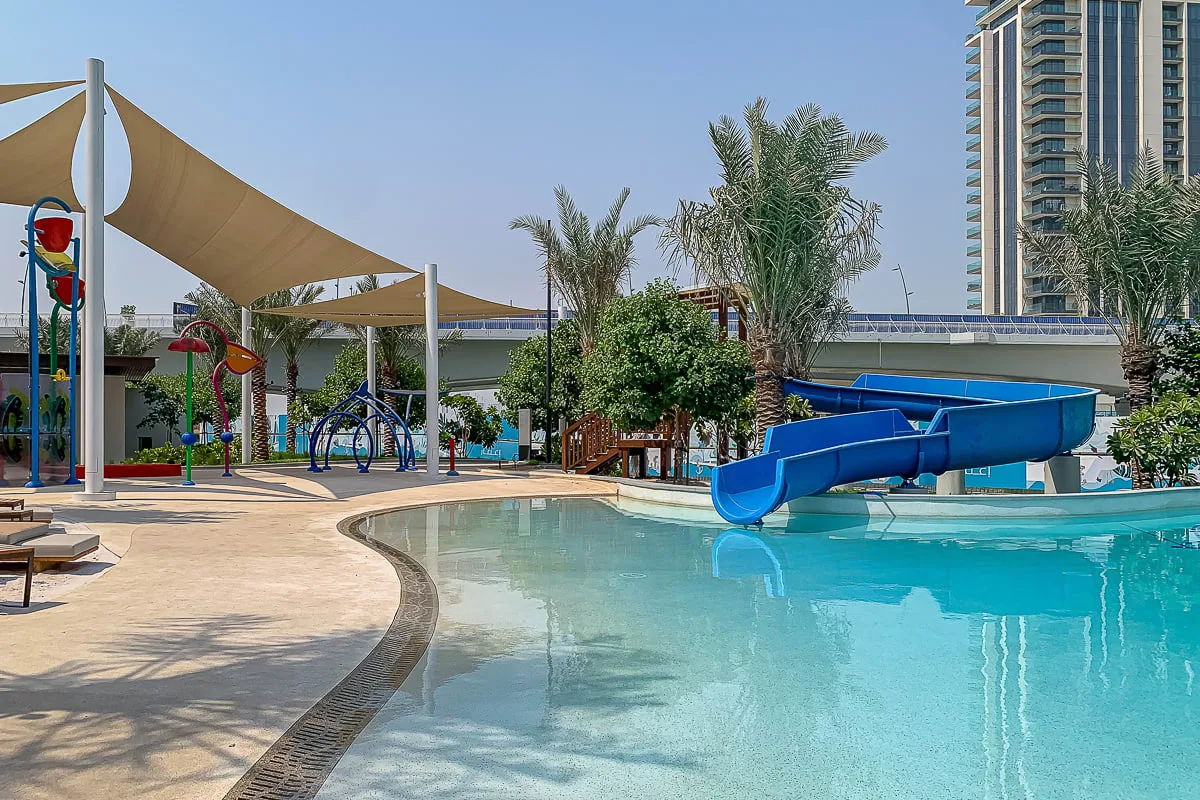An outdoor swimming pool with a blue water slide and shaded play area.