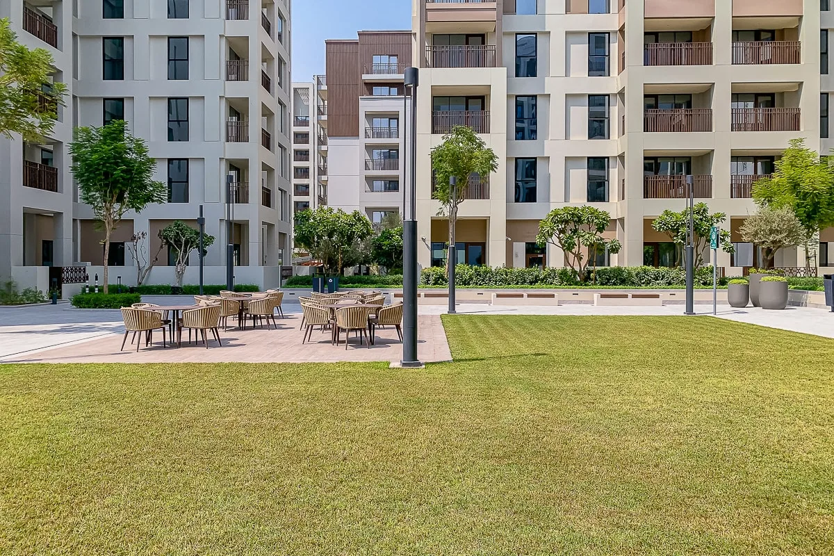 A landscaped apartment courtyard has a lawn, outdoor seating, and surrounding buildings.