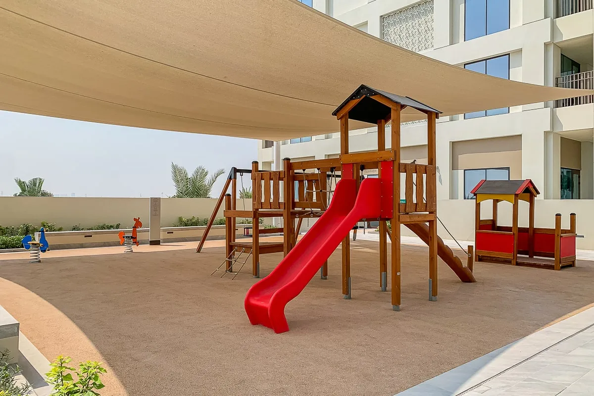 An outdoor playground with a red slide sits beneath a broad shade canopy.