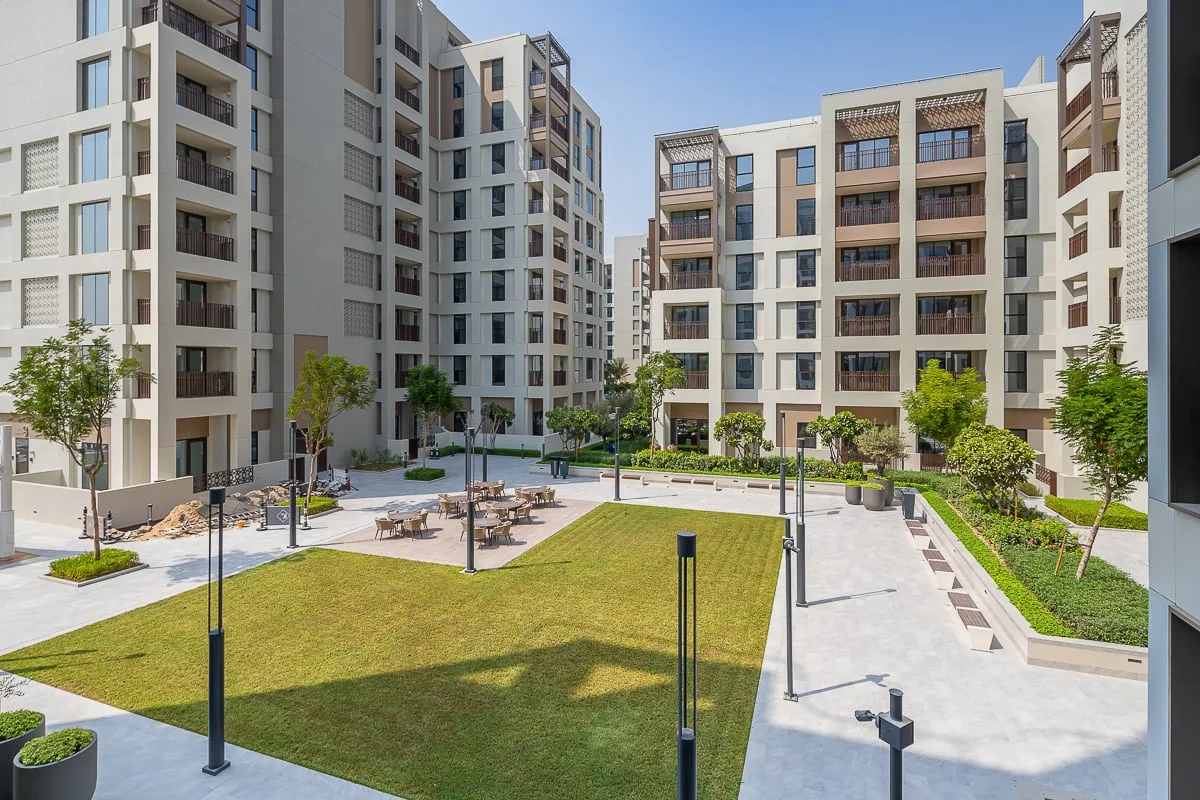 A landscaped courtyard sits among modern apartment buildings, with lawns and paved walkways.
