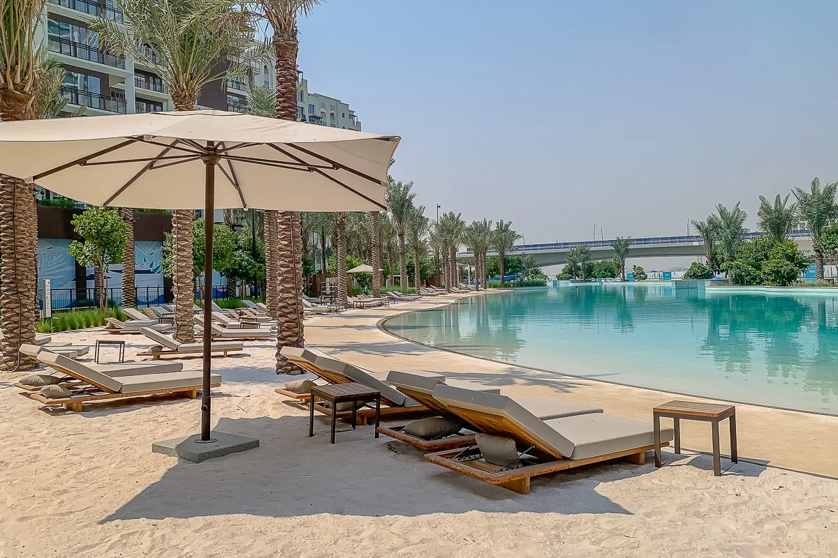 A poolside seating area with lounge chairs, umbrellas, and palm trees.