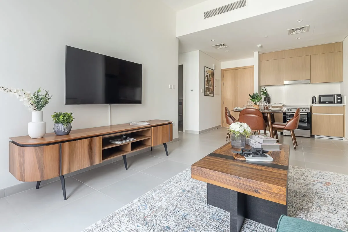 Una luminosa sala-comedor cuenta con un televisor, mesas de madera y una cocina compacta.