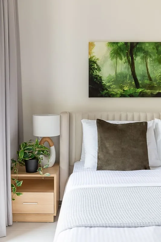 A bedroom with a neatly made bed, bedside table, and framed greenery artwork.