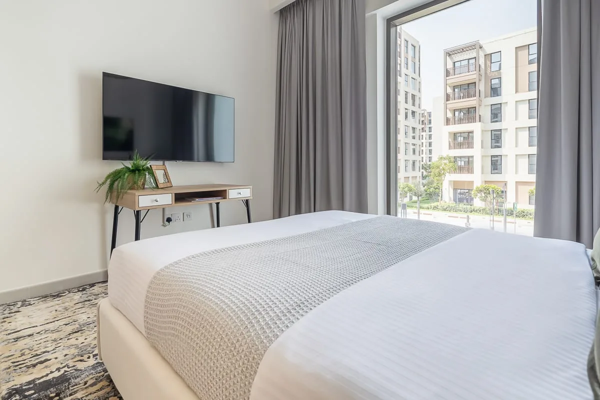 A bright bedroom with a neatly made bed and a large window.