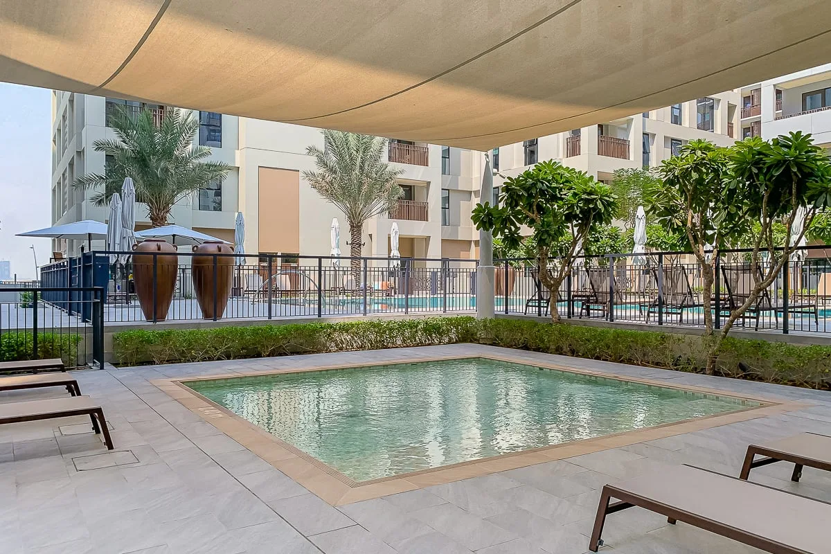 An outdoor swimming pool sits beneath a shade canopy, with lounge seating nearby.