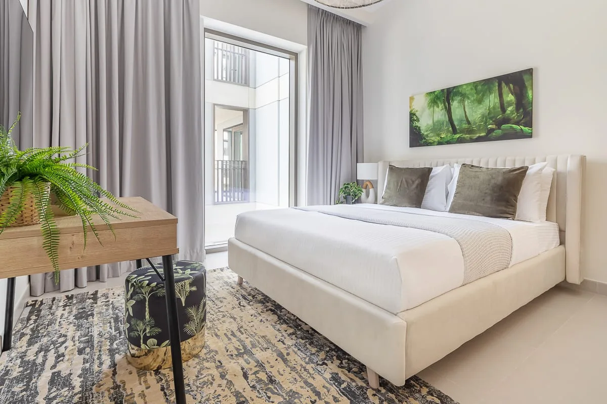 A bright bedroom with a neatly made bed beside a large window.