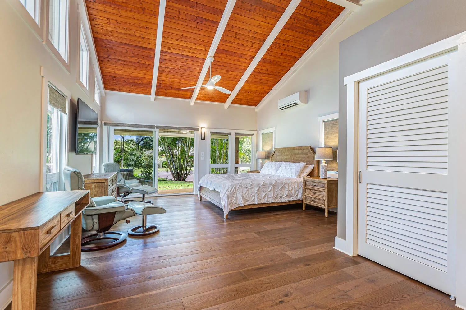 A bedroom with a bed, lounge seating, and glass doors opening to greenery.