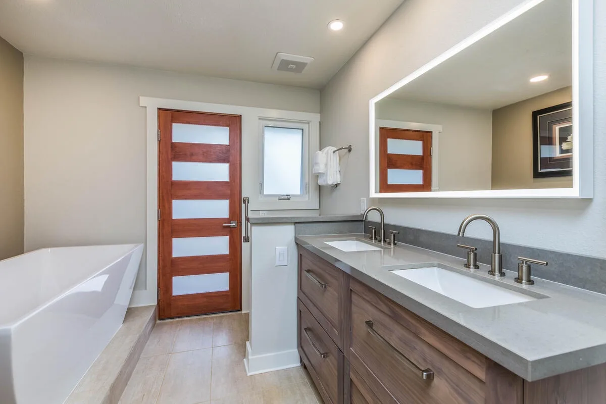 A bathroom vanity with two sinks sits beside a bathtub and a wooden door.