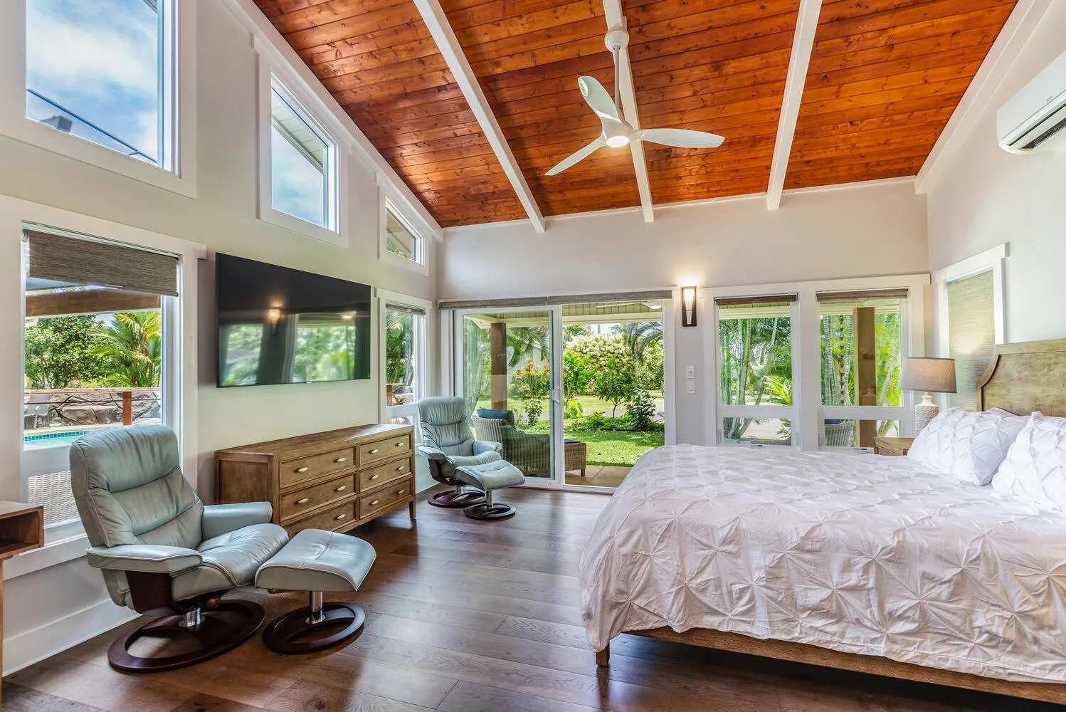 A bright bedroom with a large bed, seating, and garden views through glass doors.