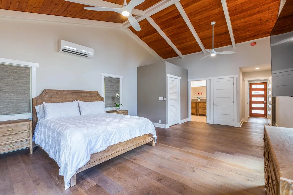 A bedroom with a bed beneath a high wood-paneled ceiling.