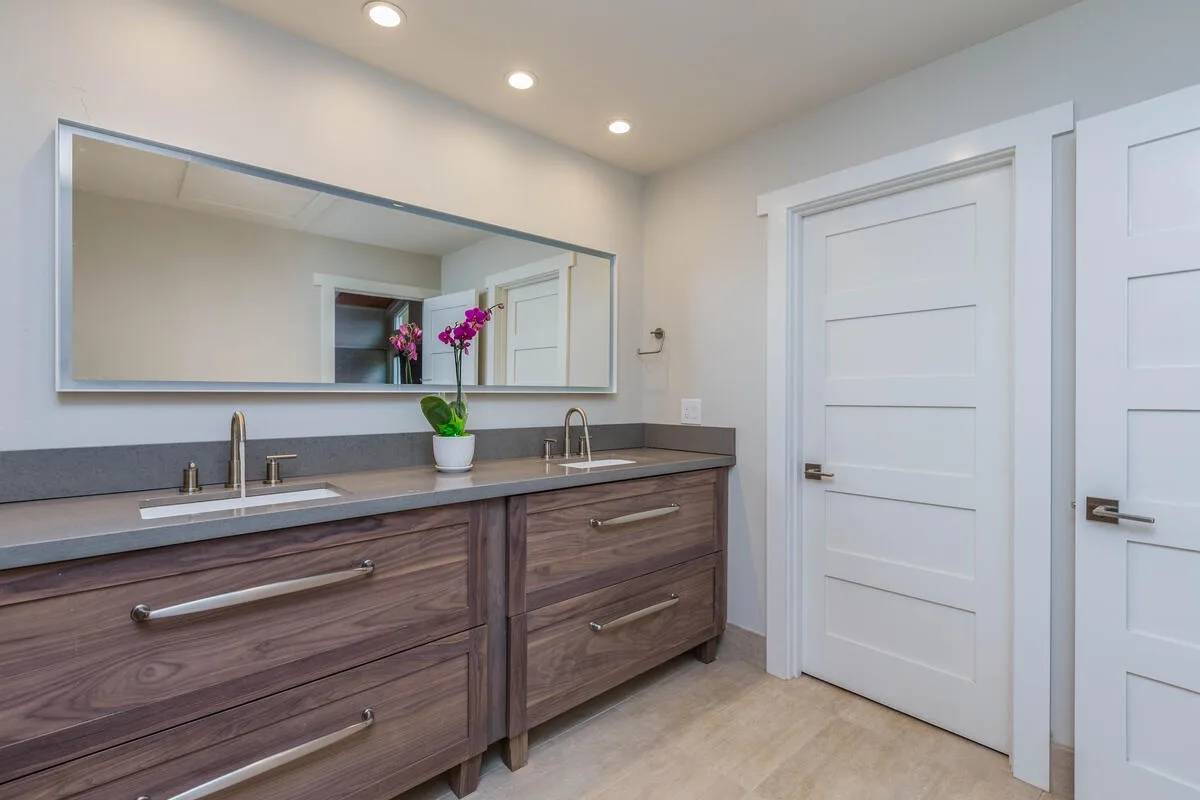 A bathroom vanity with a wide mirror, two sinks, and white paneled doors.