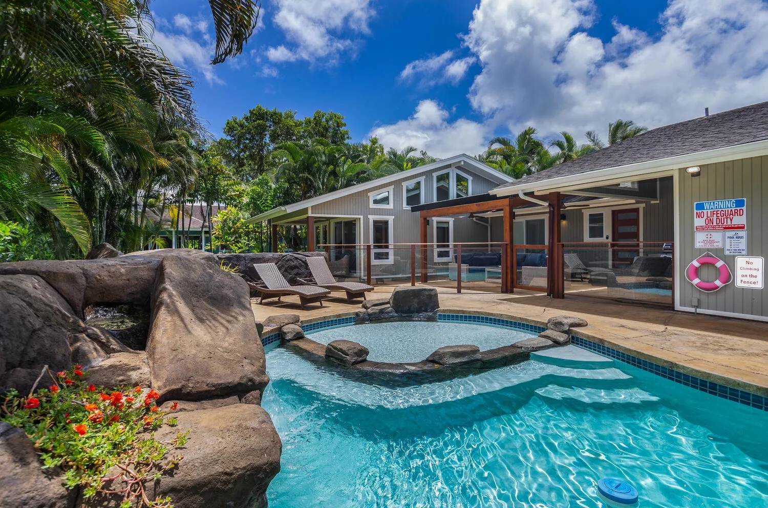 An outdoor swimming pool beside a low building, with rocks and lounge seating.
