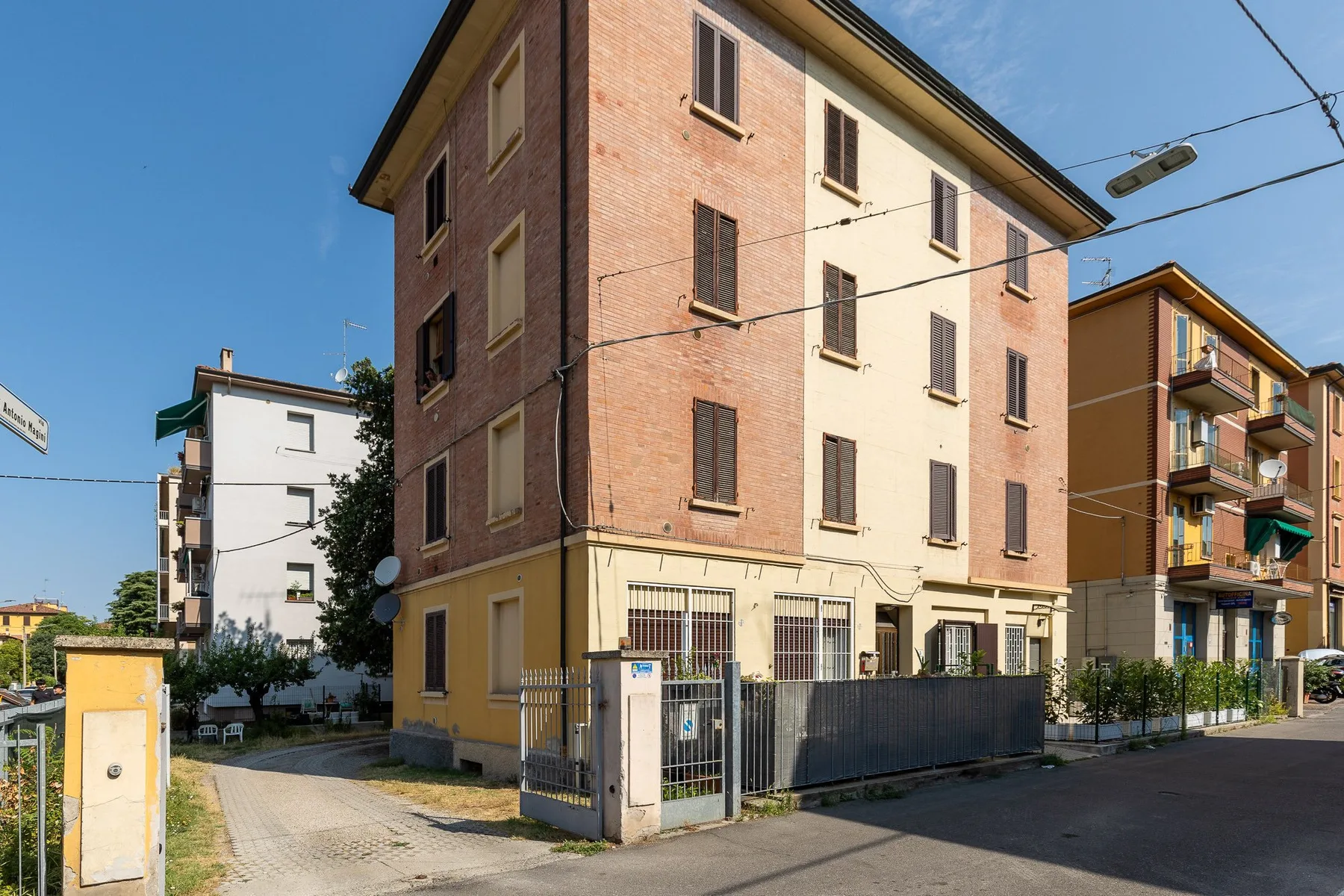A brick apartment building stands beside a paved street under a clear blue sky.