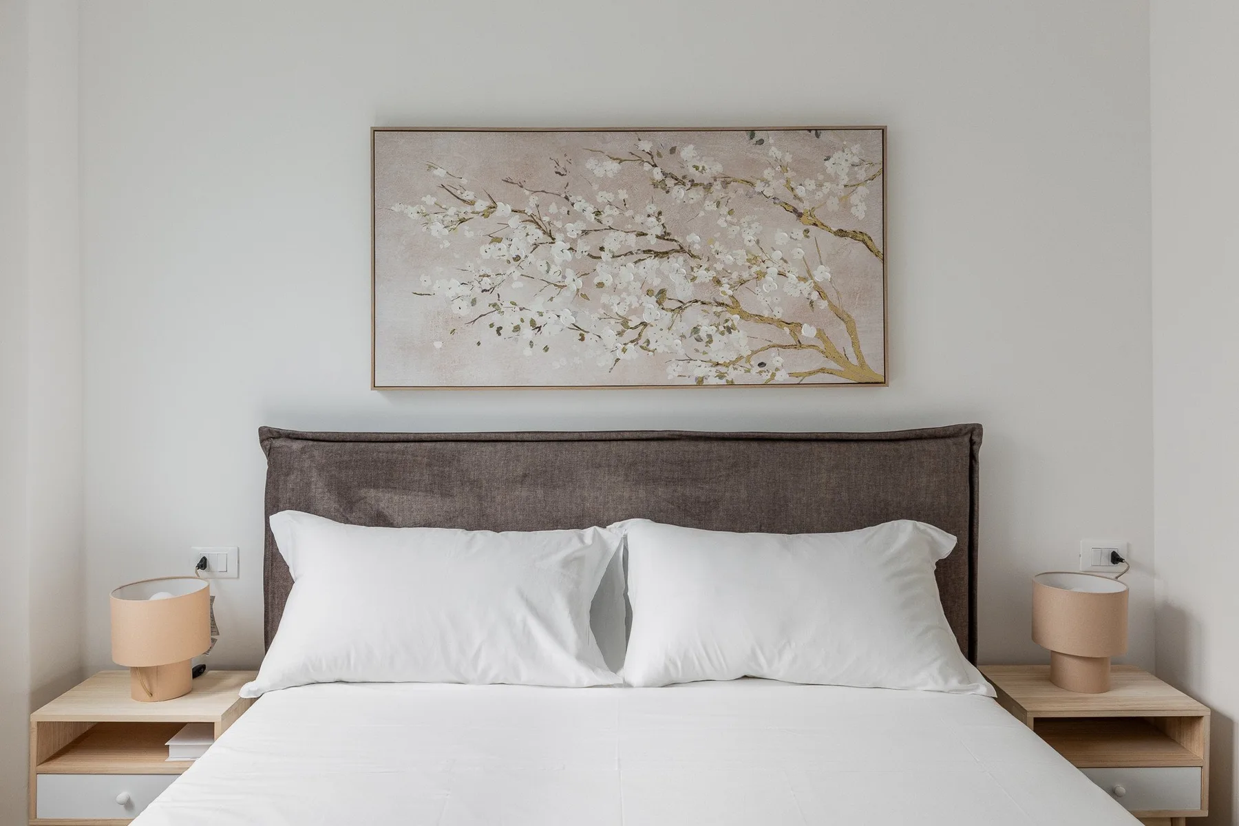 A bedroom with a bed beneath a framed floral artwork.