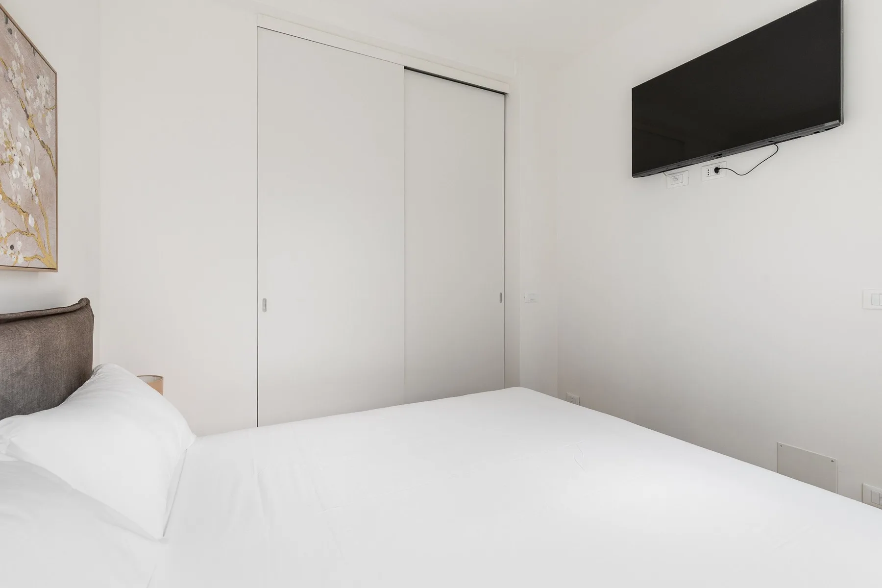 A bright bedroom with a neatly made bed and a wall-mounted television.