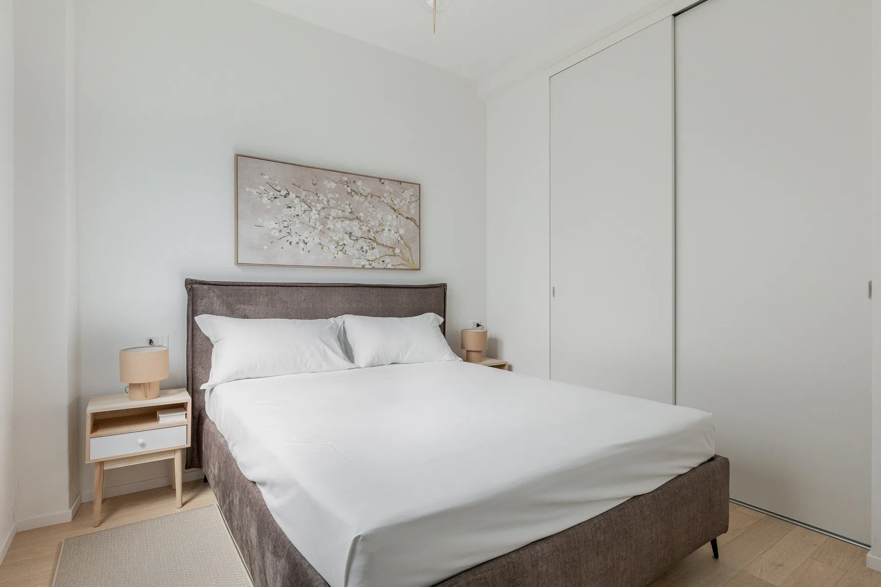 A bright bedroom with a neatly made bed and framed artwork above it.