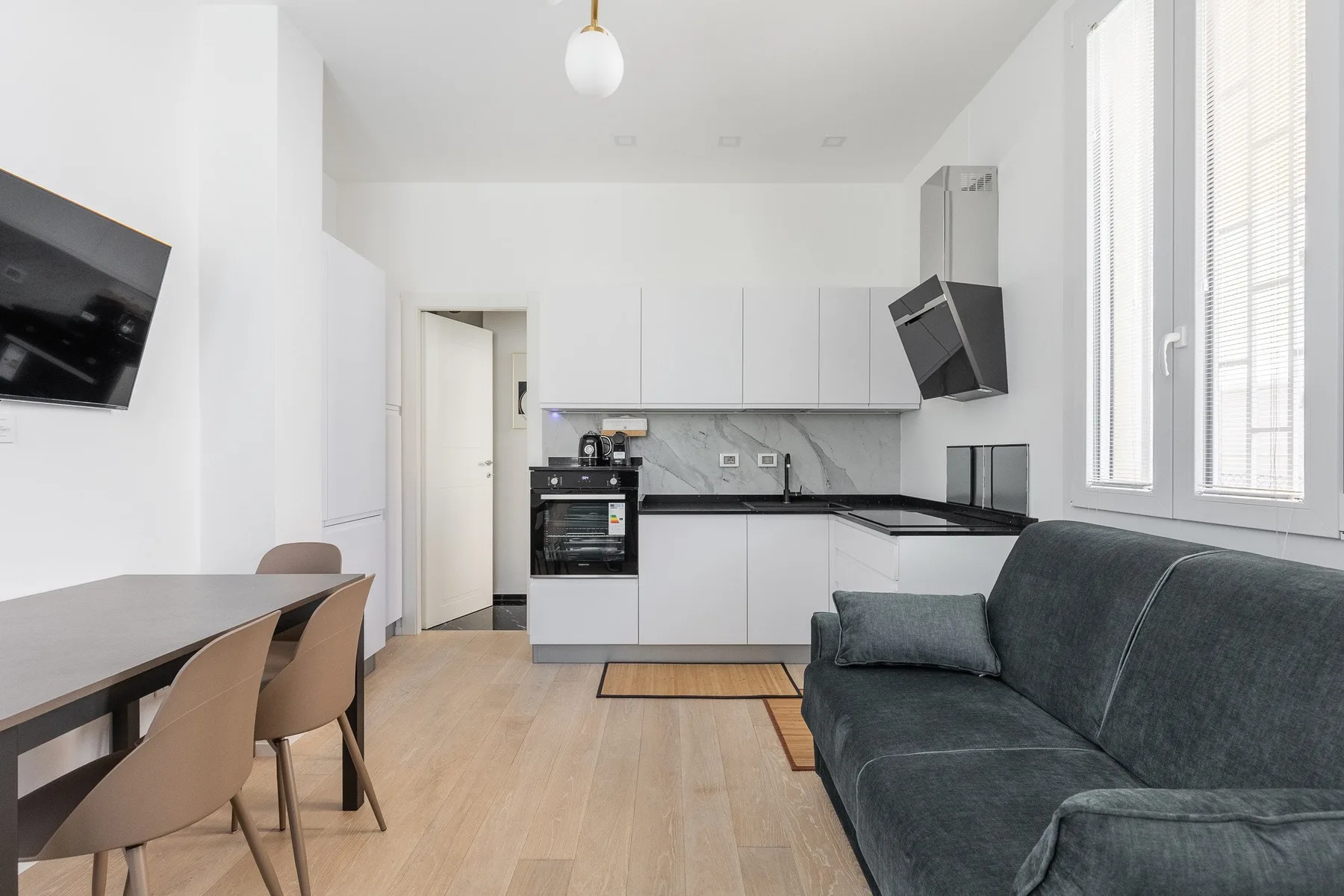 A bright living room and kitchen with a dining table beside the windows.