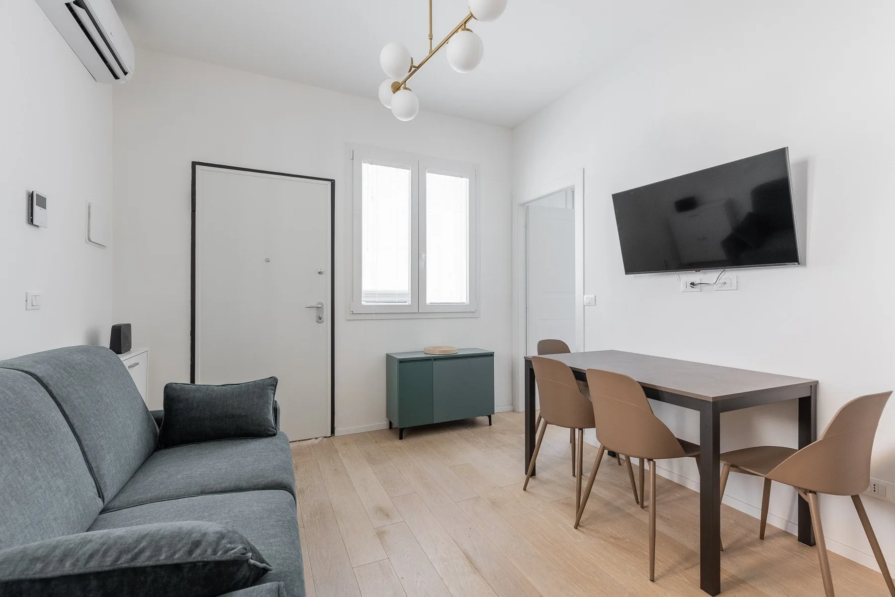 A bright living and dining area with seating, a table, and a wall-mounted television.