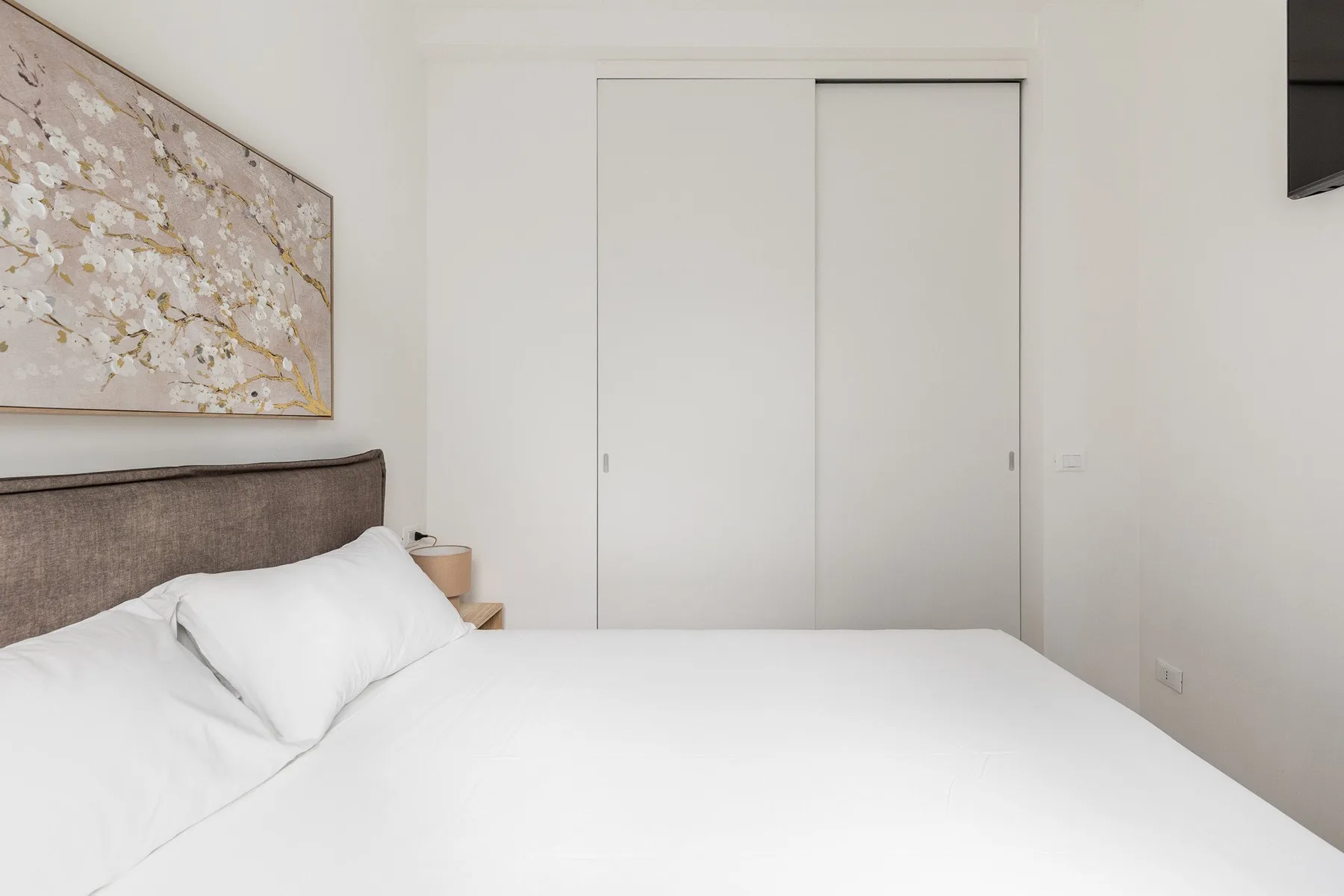A bright bedroom with a neatly made bed and sliding closet doors.