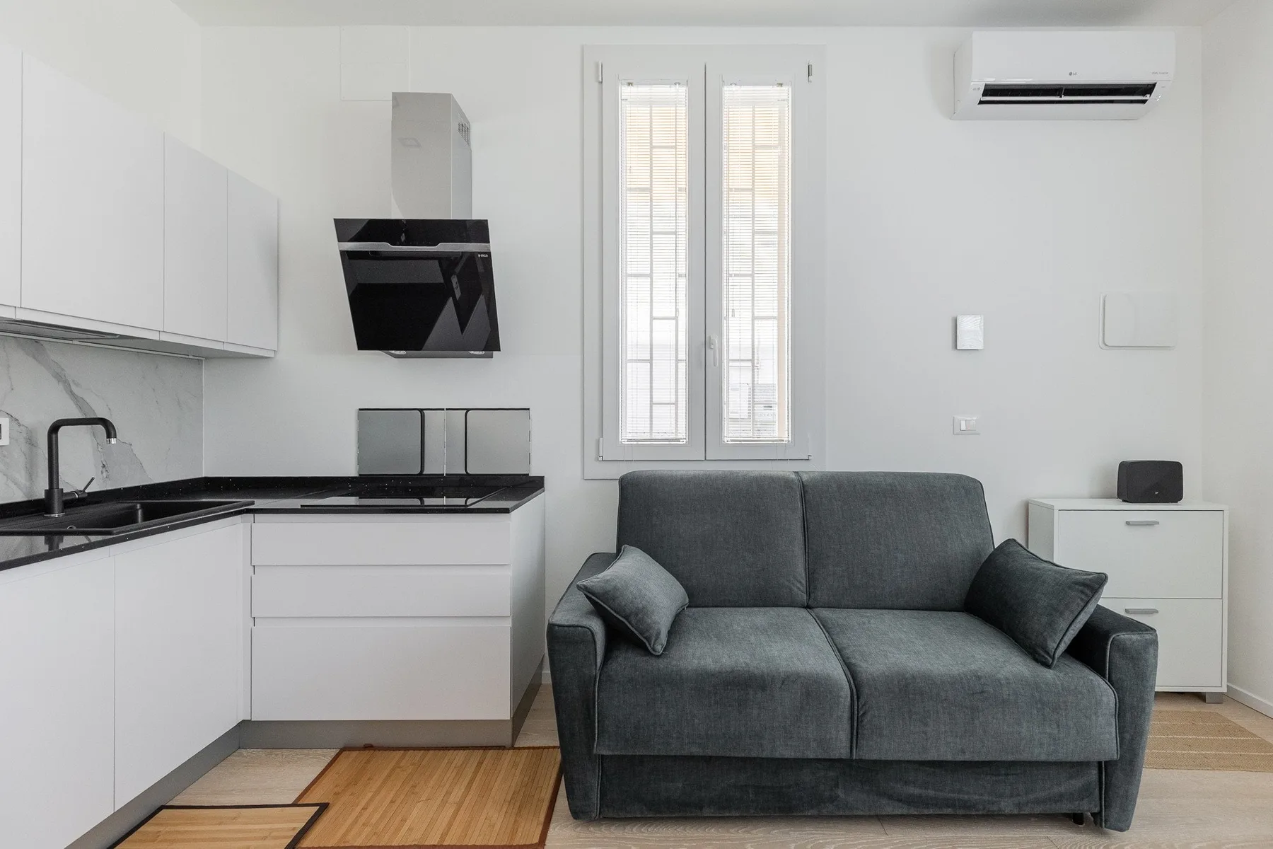 A bright living area with a gray sofa beside a compact kitchen.