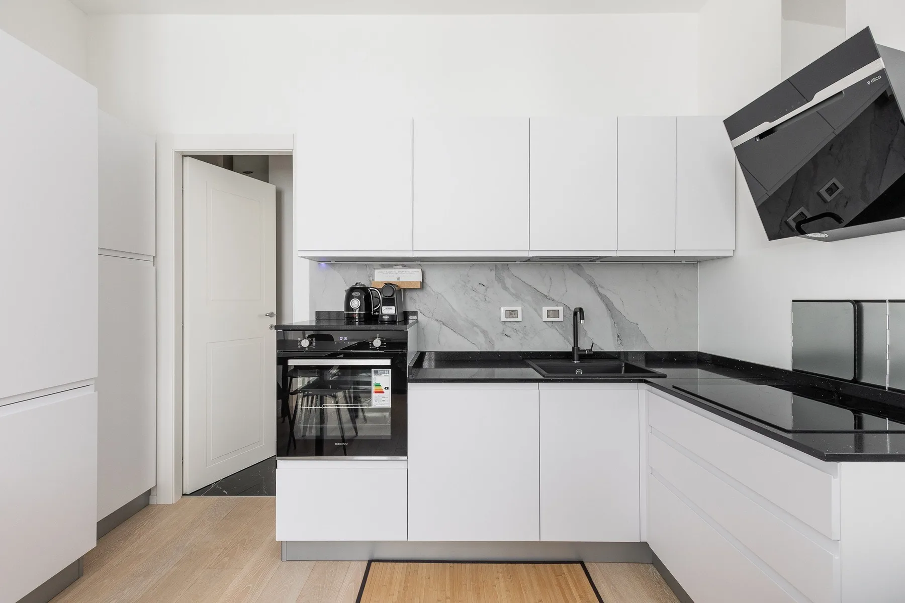 A modern kitchen with white cabinets, dark countertops, and built-in appliances.