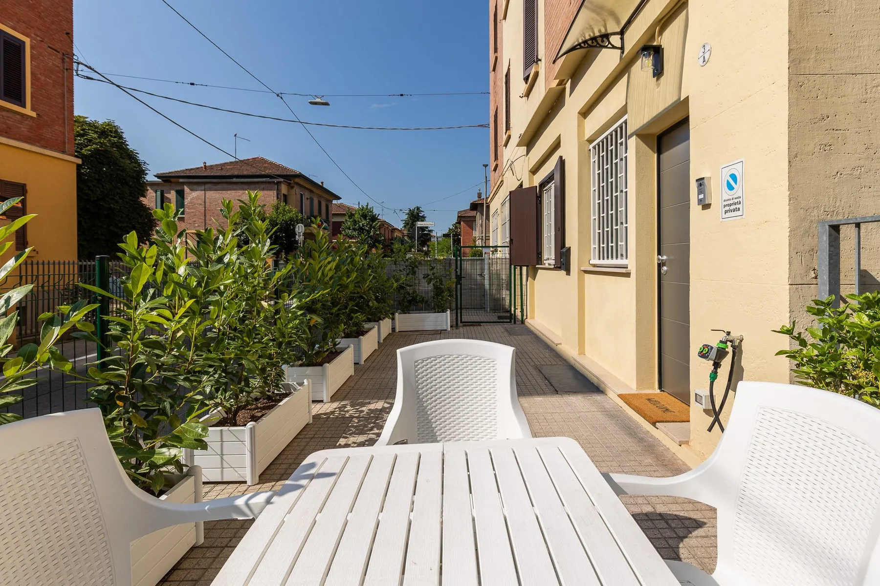 An outdoor patio with a white table and chairs beside a yellow building.