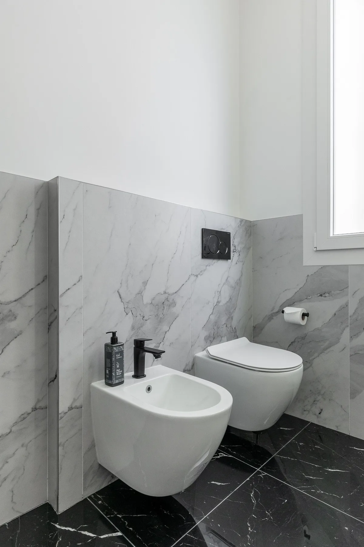 A modern bathroom with a wall-mounted sink, toilet, and marble-patterned walls.