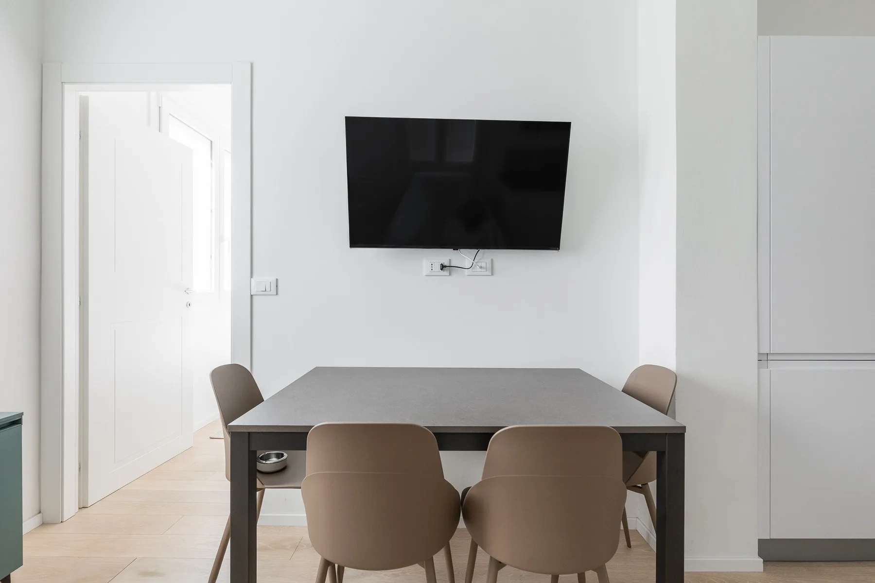 A dining area with a table and seating beneath a wall-mounted television.