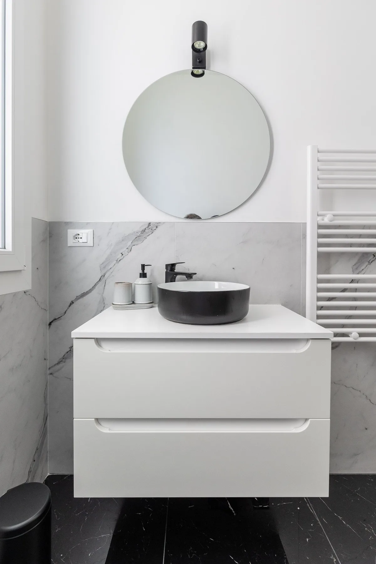 A modern bathroom vanity with a round mirror and black vessel sink.