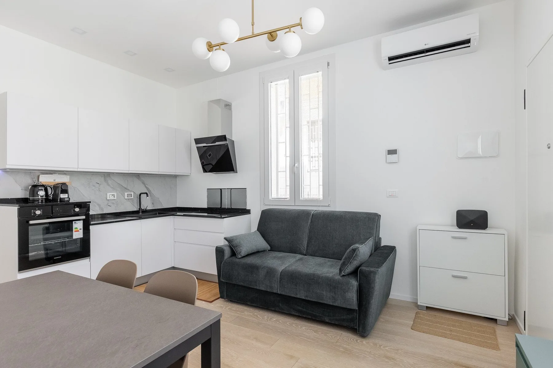Una pequeña sala de estar con un sofá gris junto a una cocina.