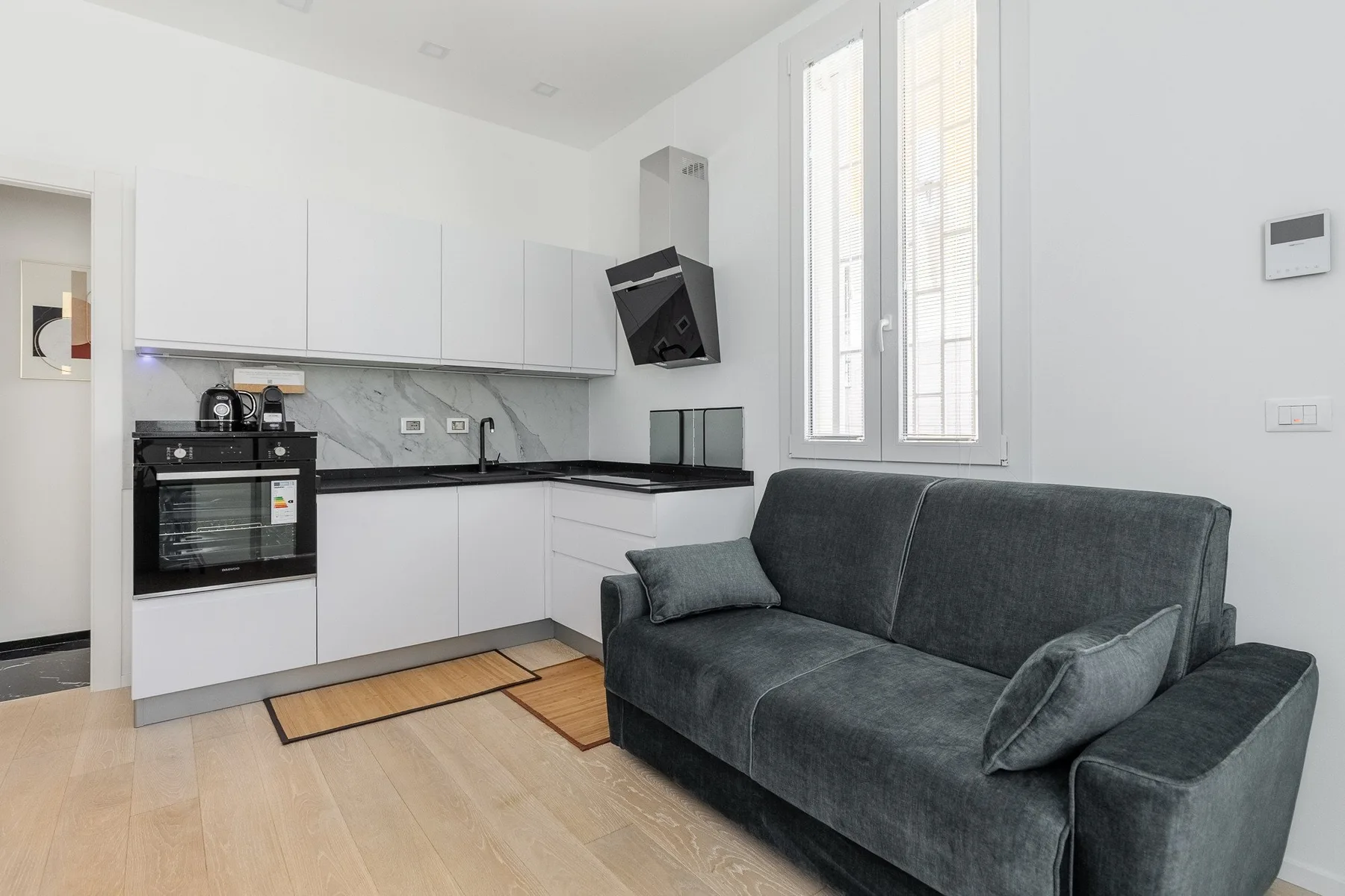 A bright kitchen and living area with white cabinets and a dark sofa.