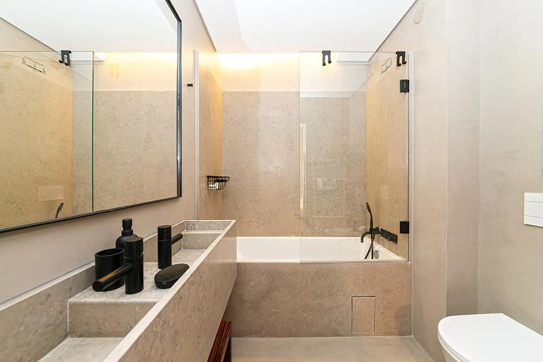 Un baño luminoso con bañera, paneles de vidrio y un lavabo alargado.