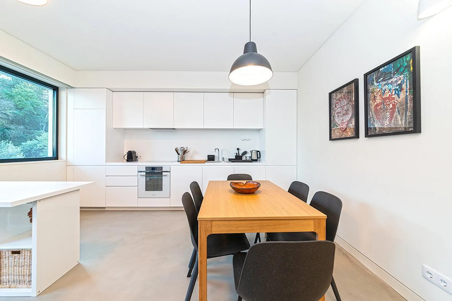 Una cocina y comedor luminosos con una mesa de madera y armarios blancos.