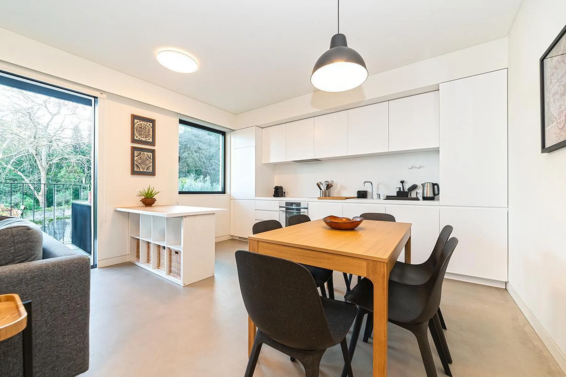 Una cocina moderna con comedor, mesa de madera y armarios blancos.