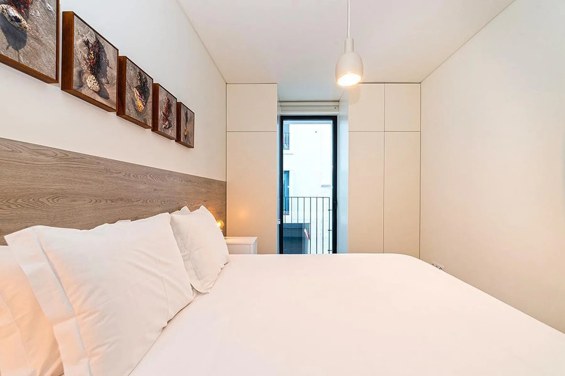 Un dormitorio luminoso con una cama bien tendida y cuadros en la pared.