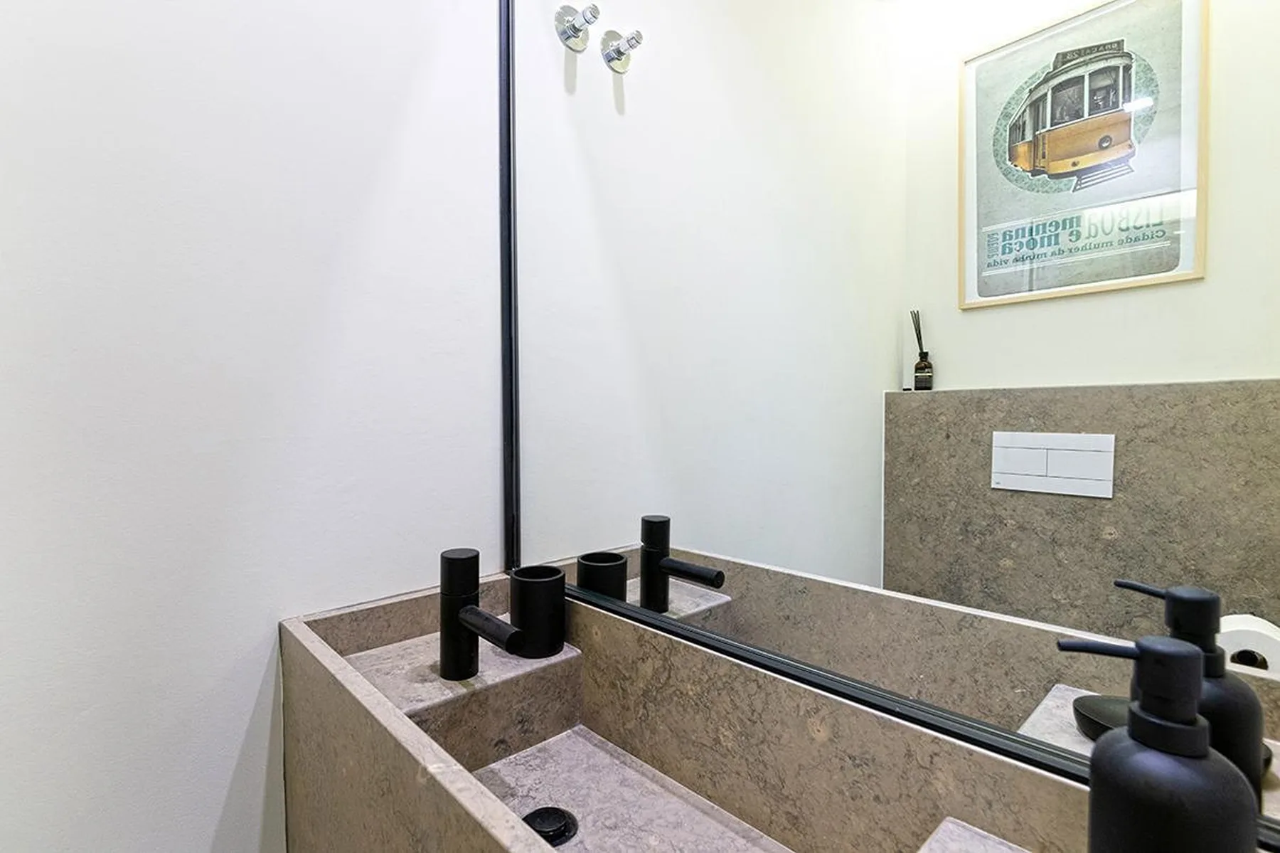 Un lavabo de baño con encimera de piedra, grifos negros y un espejo grande.