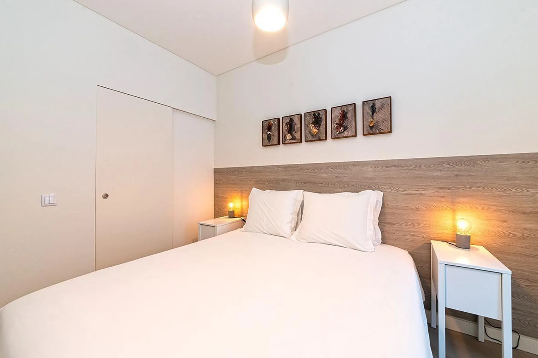 Un dormitorio con una cama, cuadros y mesitas de noche.