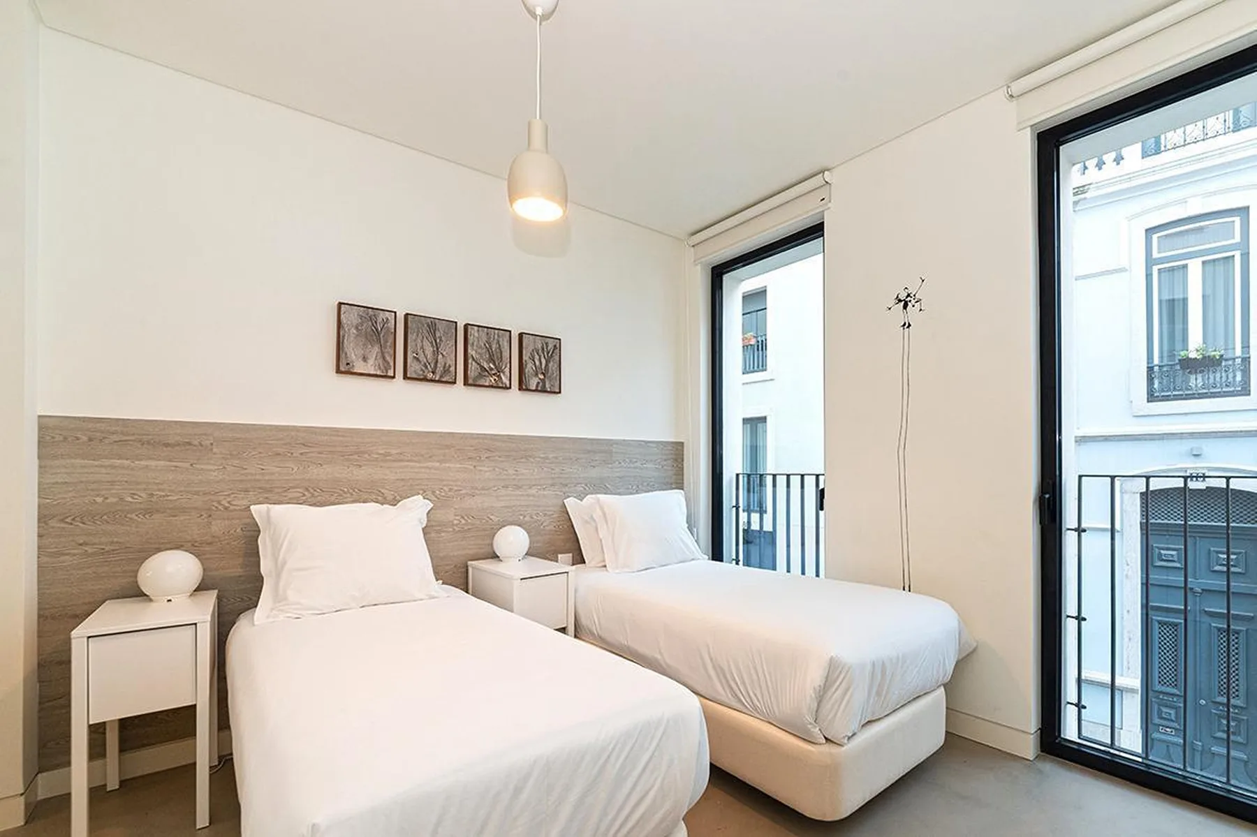 Un dormitorio luminoso con dos camas, mesitas de noche y ventanas grandes.